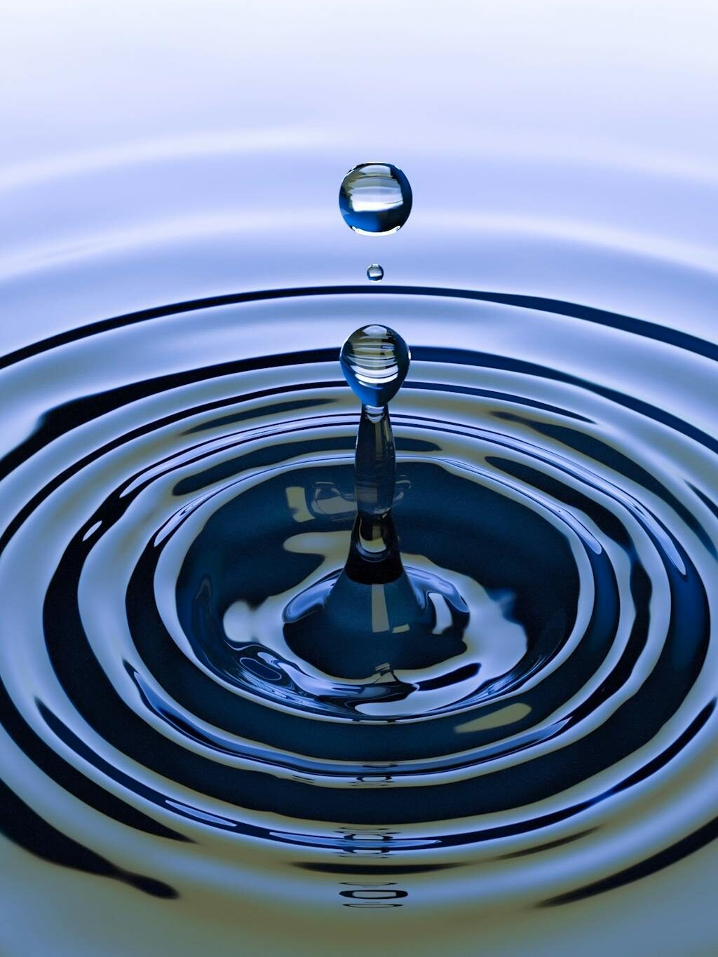 A stunning close-up of a water droplet creating ripples on a smooth water surface, capturing nature's simplicity.