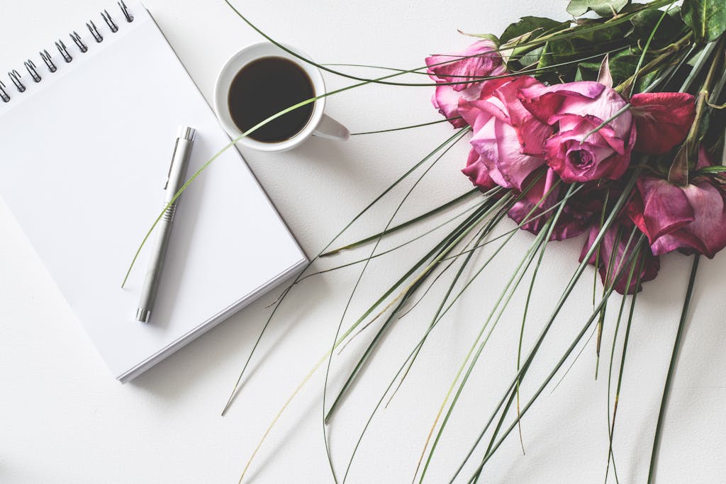 A stylish composition of pink roses, a cup of coffee, and a notepad. Perfect for romantic themes.