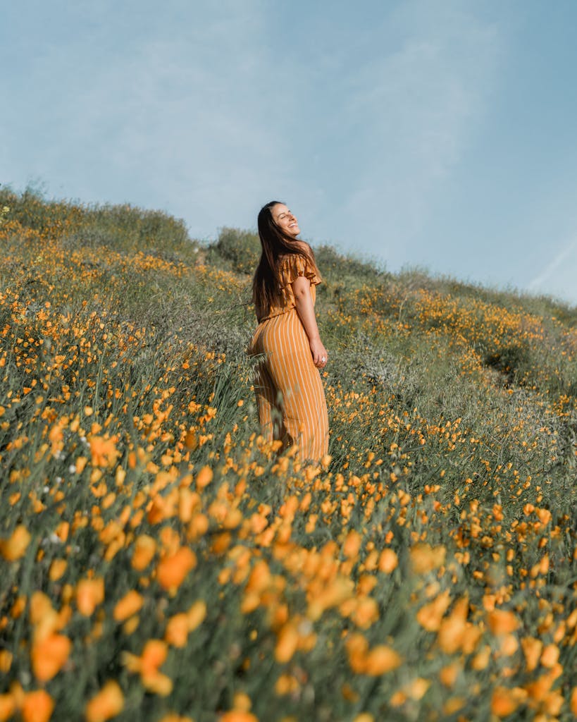 A woman in a yellow dress smiles amidst lush poppy fields in Lake Elsinore, capturing the joy of a superbloom.