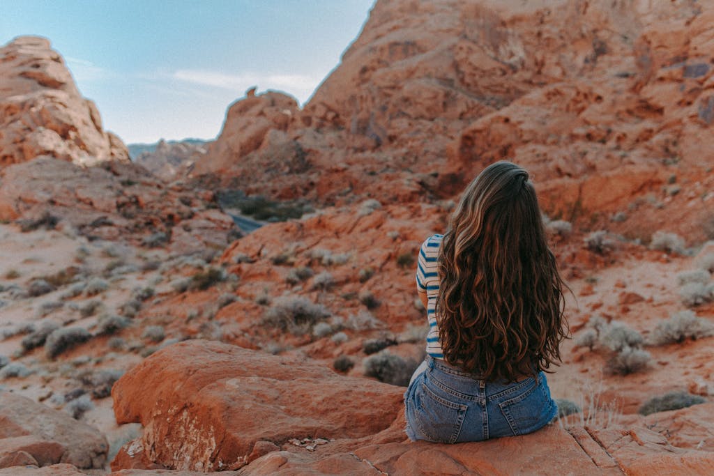 A woman sits thoughtfully on red rocks in Nevada's Valley of Fire, embracing nature's beauty.