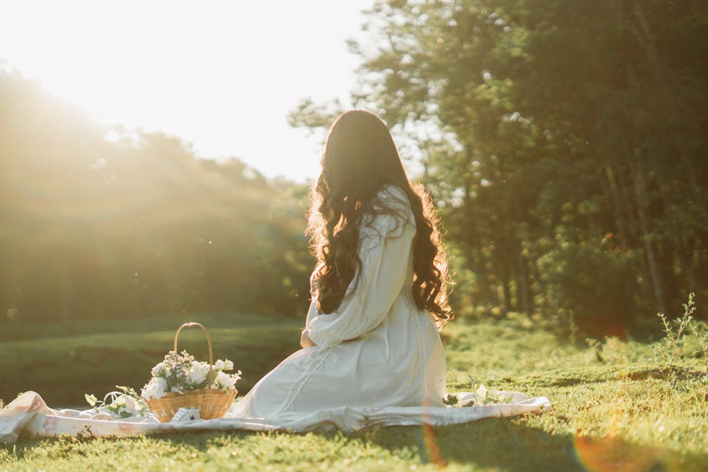 A woman sitting leisurely on grass in sunlight with flowers and basket, embracing nature.