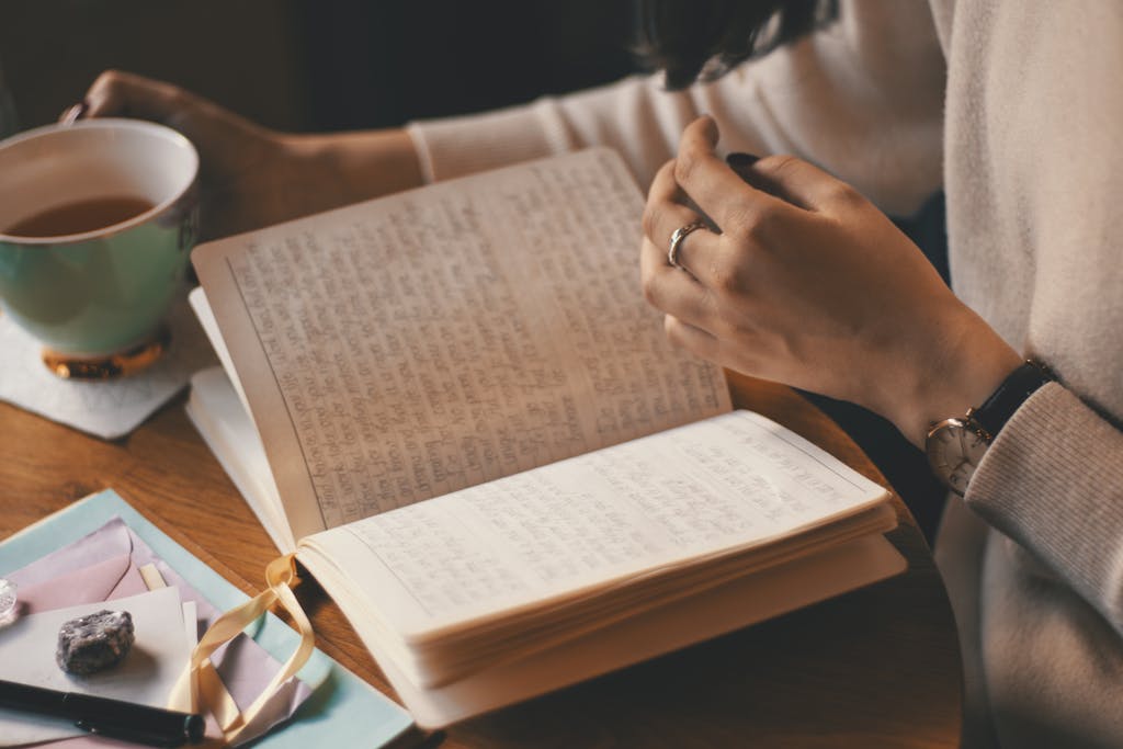 A woman writes in a journal while enjoying a cup of coffee at a wooden table.