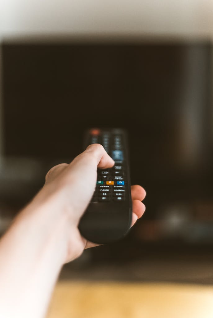 Close-up of a hand using a remote control to operate a TV, emphasizing modern technology.