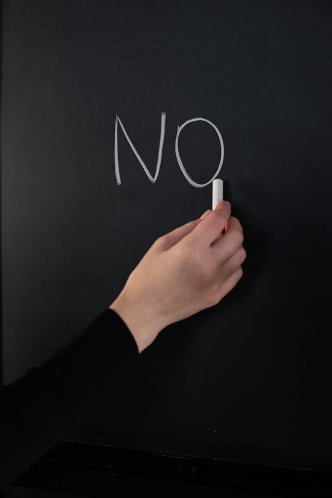 Close-up of a hand writing 'NO' on a chalkboard using white chalk.