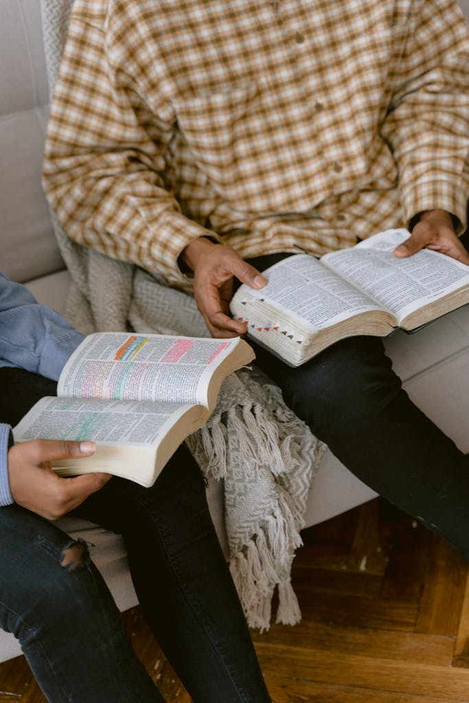 Two individuals sitting on a sofa reading and discussing the Bible indoors.