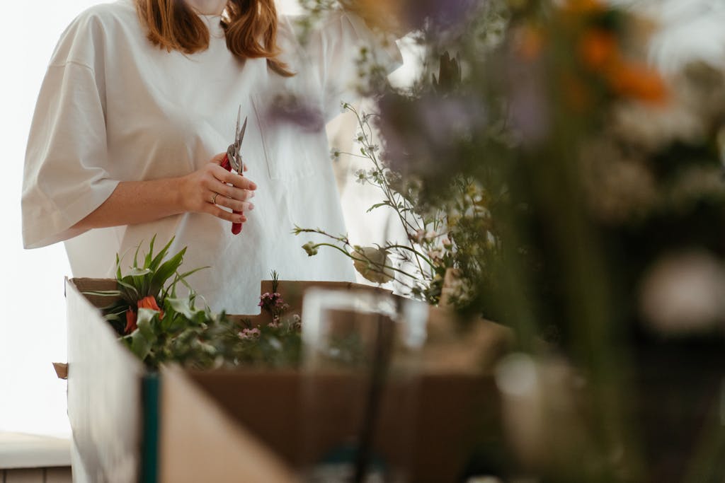 Woman arranging fresh flowers using scissors indoors. Perfect for floral arrangement and gardening themes.