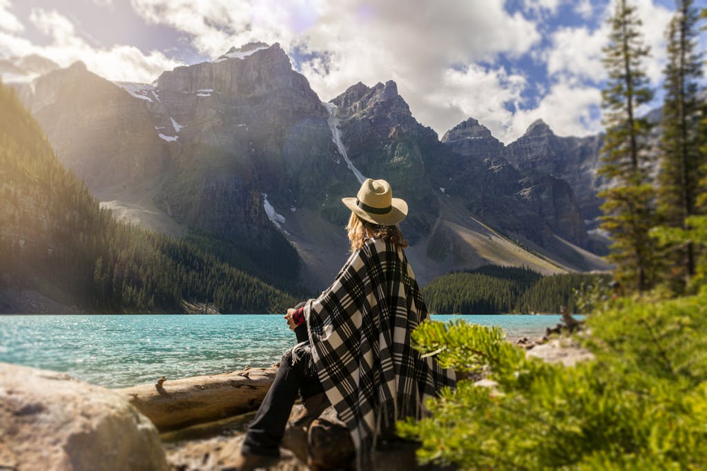 Woman in a poncho gazing at Moraine Lake surrounded by mountains, Alberta, Canada.