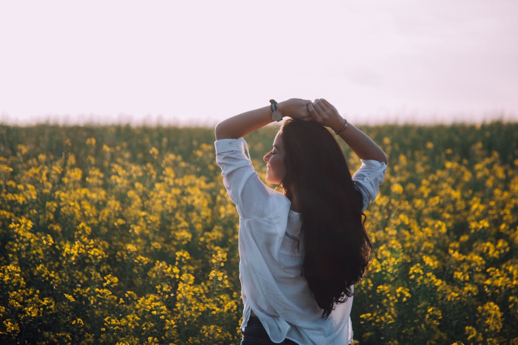 Woman in white shirt enjoying a sunny day in a blooming flower field.