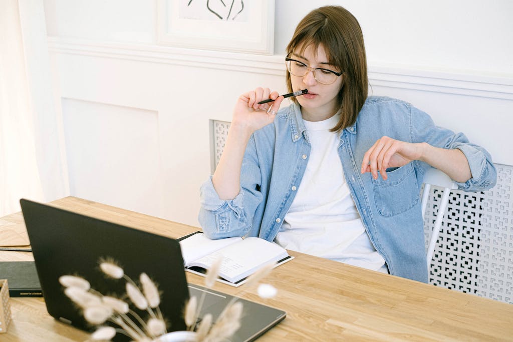 Woman working thoughtfully in home office, reflecting on ideas with laptop and notebook.